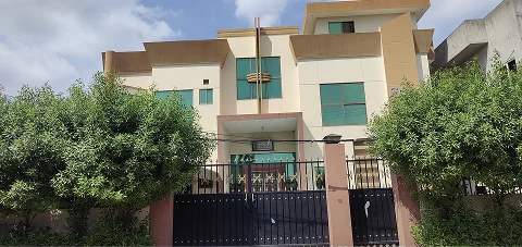Exterior view of a modern garment factory building with trees and a black gate